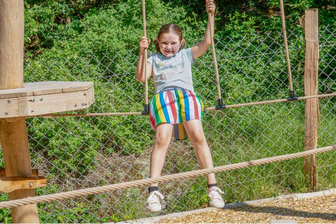 Ein Mädchen hat Spaß am Schaukeln im Abenteuerwald Elsass.